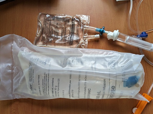 Two IV fluid bags. One is spiked, one is still in packaging.